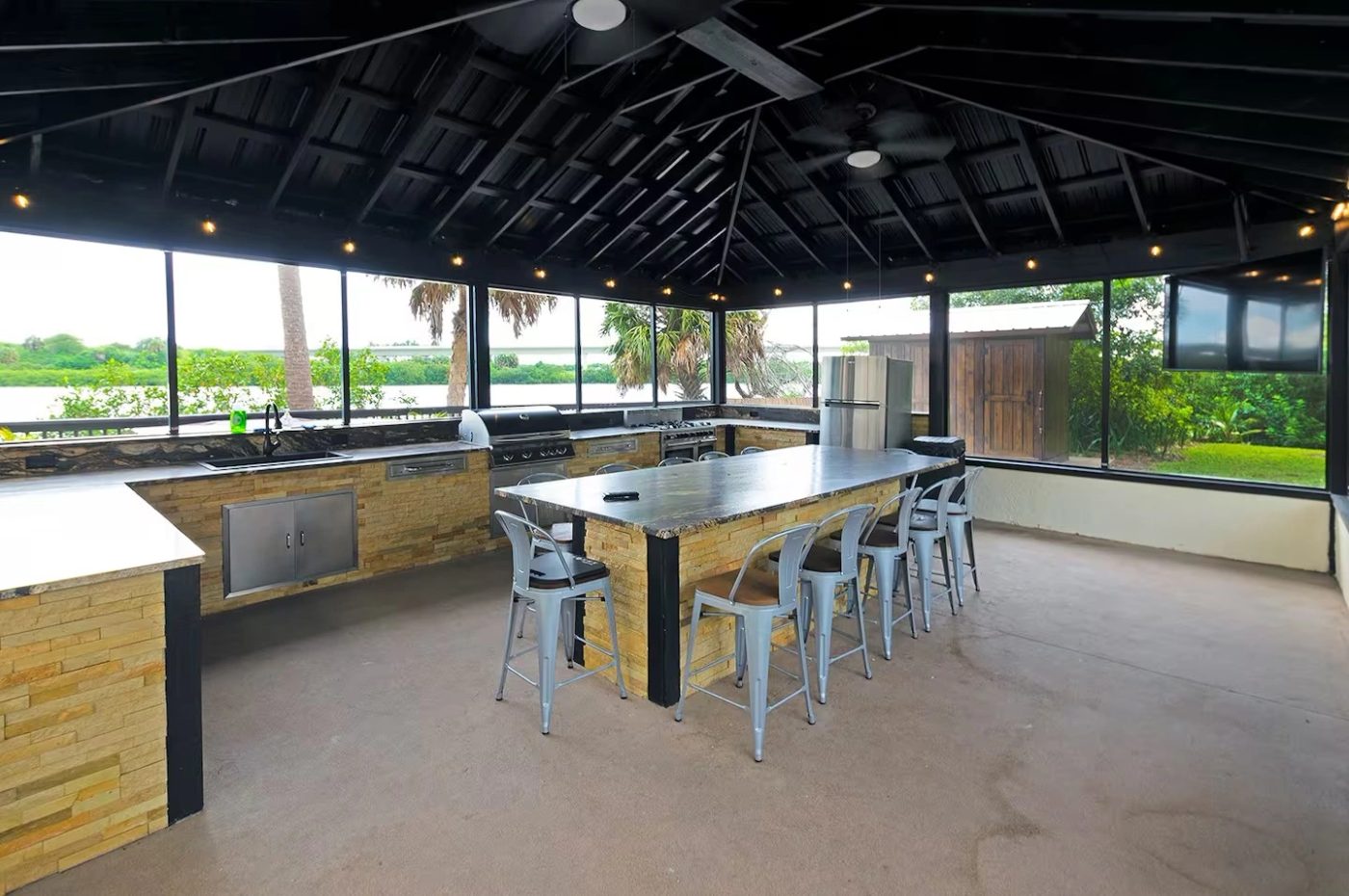 Covered waterfront outdoor kitchen with a long stone bar top and bar seating