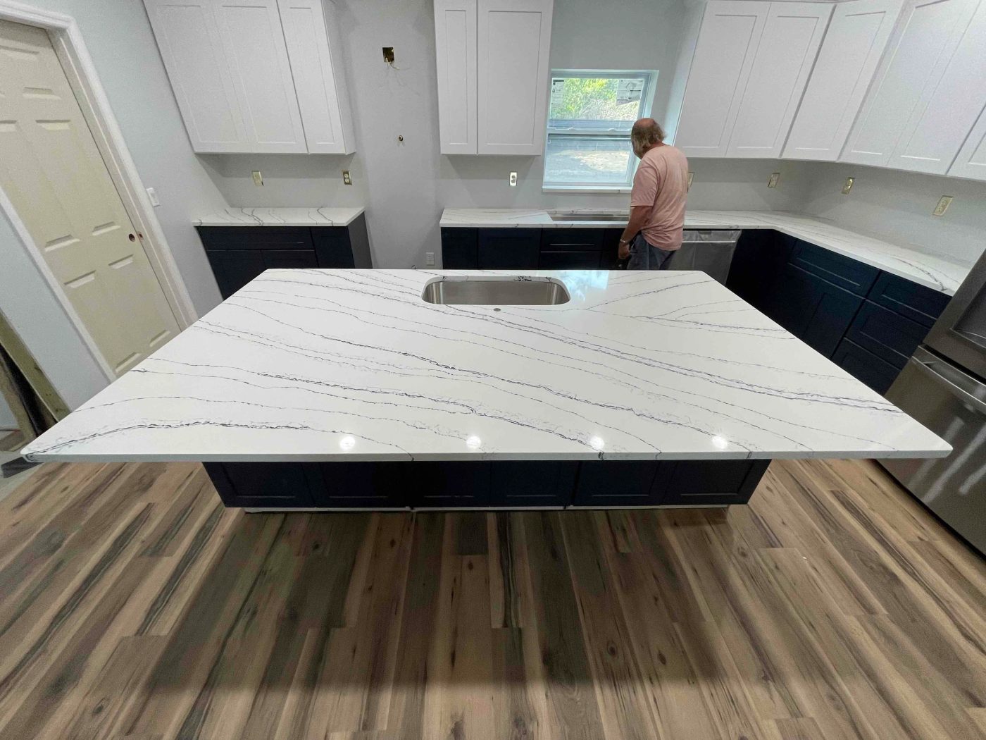 Large white quartz island with grey veining installed over navy shaker cabinets